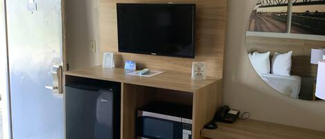 Une chambre d’hôtel équipée d’un lit, d’un bureau avec un ordinateur, d’une télévision, d’un mini-bar et d’un miroir.
