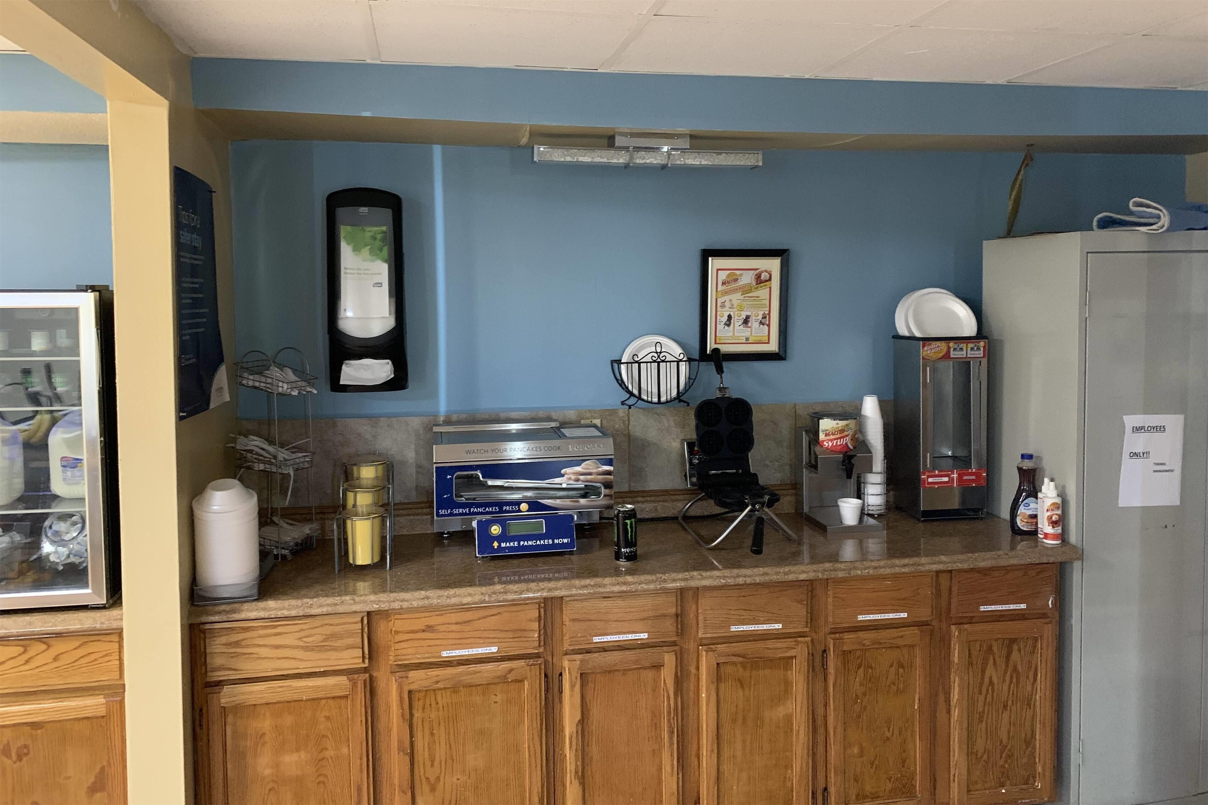 A kitchen area with a self-serve breakfast station, including a coffee machine, a waffle maker, and a refrigerator.