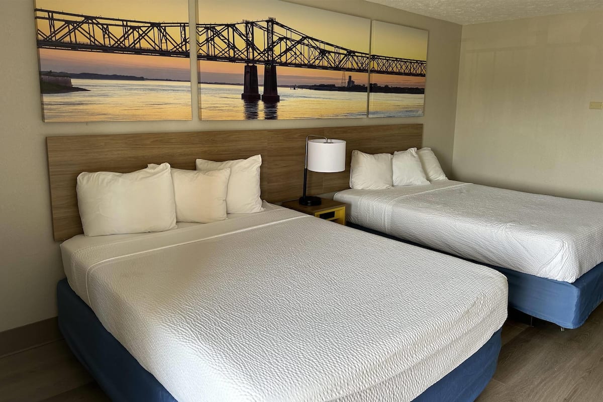 Une chambre d’hôtel avec deux lits, une table de chevet, une lampe et un grand tableau représentant un pont.