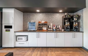 Una cocina moderna con gabinetes blancos, microondas, un cubo de basura, una estación de café con dos cafeteras y un salpicadero decorativo.