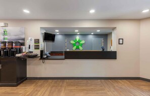 A reception area with a counter, a digital screen, a green decorative element, and a sign indicating office hours. - Extended Stay America Suites Washington DC Centreville Manas (Centreville)