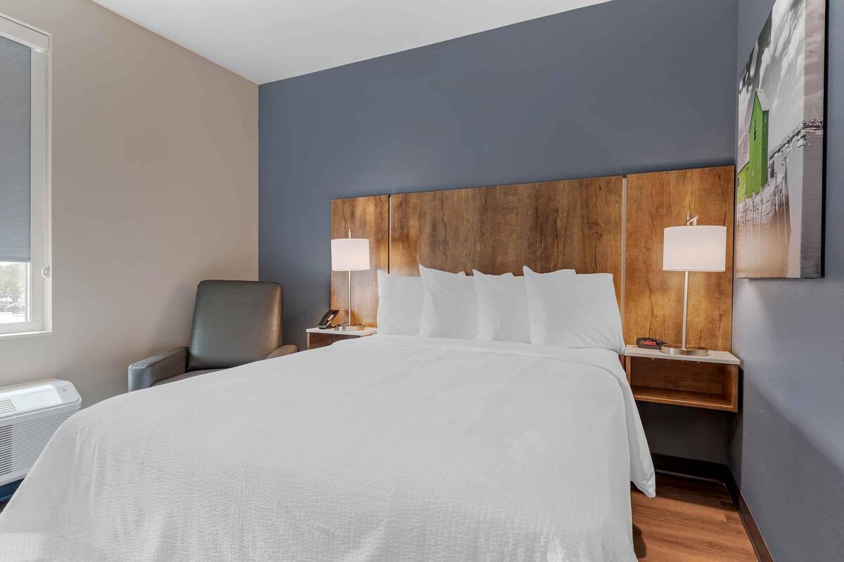 A hotel room with a large bed, two bedside tables with lamps, a chair, and a wall-mounted artwork.