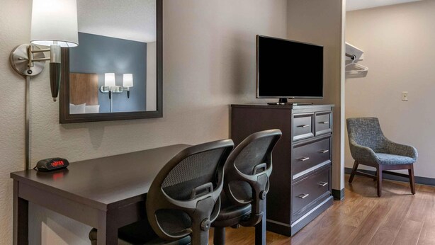 Habitación de hotel con escritorio, dos sillas, televisor, espejo y lámpara de pared.