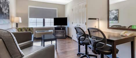 A hotel room with a sofa, a desk with two chairs, a television, a desk lamp, a phone, and a large mirror.