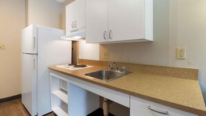 A compact kitchen with white cabinets, a stainless steel sink, and a built-in refrigerator. - Extended Stay America Suites Washington DC Centreville Manas (Centreville)