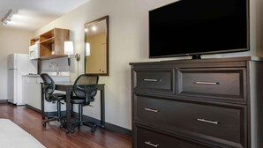 A hotel room with a kitchenette, a desk with two chairs, a large flat-screen TV, and a dark-colored dresser. - Extended Stay America Suites Washington DC Centreville Manas (Centreville)
