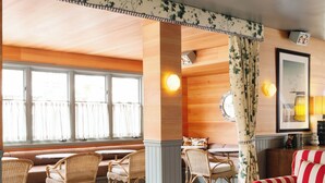 A cozy room with a wooden ceiling, a round table with a glass jar, striped sofas, and wicker chairs. - Le Petit Pali at 8th Ave (Carmel)