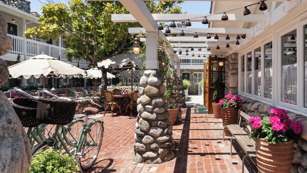 A patio area with a stone pillar, wicker chairs, a bicycle, and potted plants.