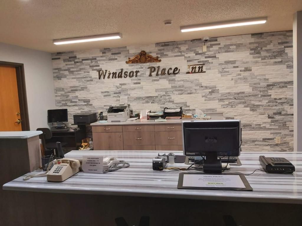 A reception desk with a stone wall backdrop, a computer, a telephone, and a sign indicating the name 'Windsor Place Inn'.