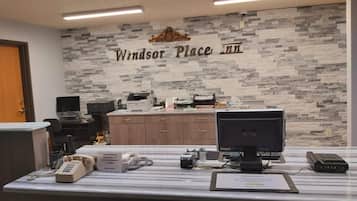 A reception desk with a stone wall backdrop, a computer, a telephone, and a sign indicating the name 'Windsor Place Inn'.