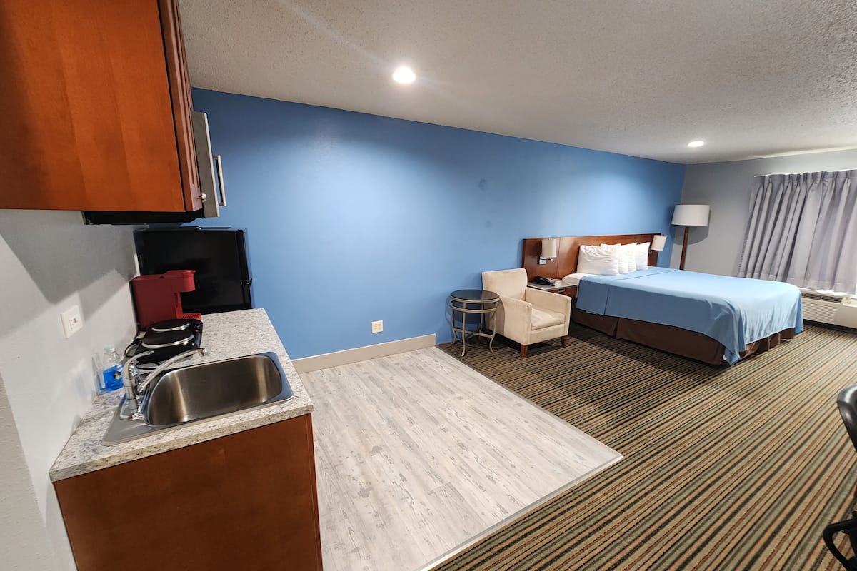 A hotel room with a kitchenette, a bed, a chair, and a small table.