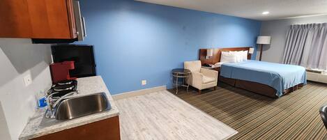 A hotel room with a kitchenette, a bed, a chair, and a small table.