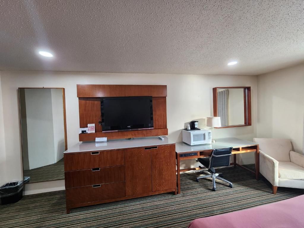 A hotel room with a wooden desk, a television, a microwave, a chair, and a bed.