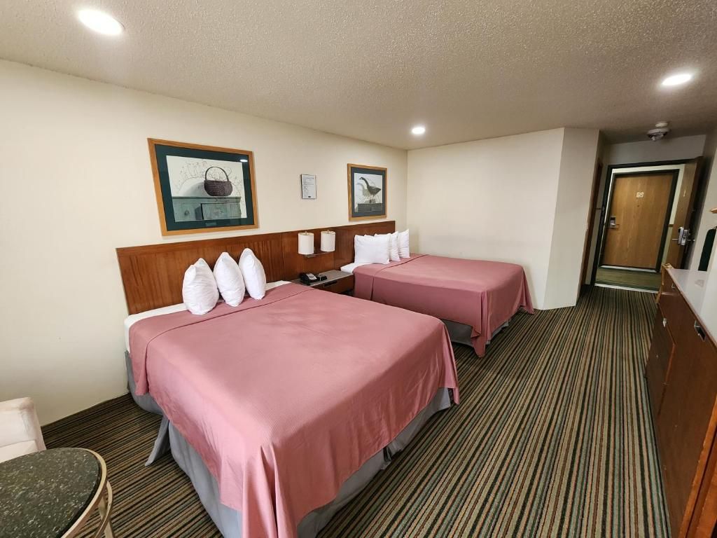 A hotel room with two beds, a wooden headboard, a striped carpet, and a door to the right.