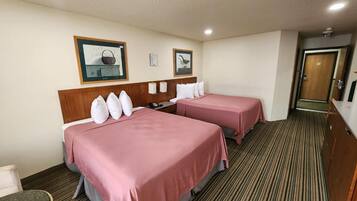 A hotel room with two beds, a wooden headboard, a striped carpet, and a door to the right.