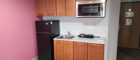 A kitchen with wooden cabinets, a black refrigerator, a microwave, and a sink.