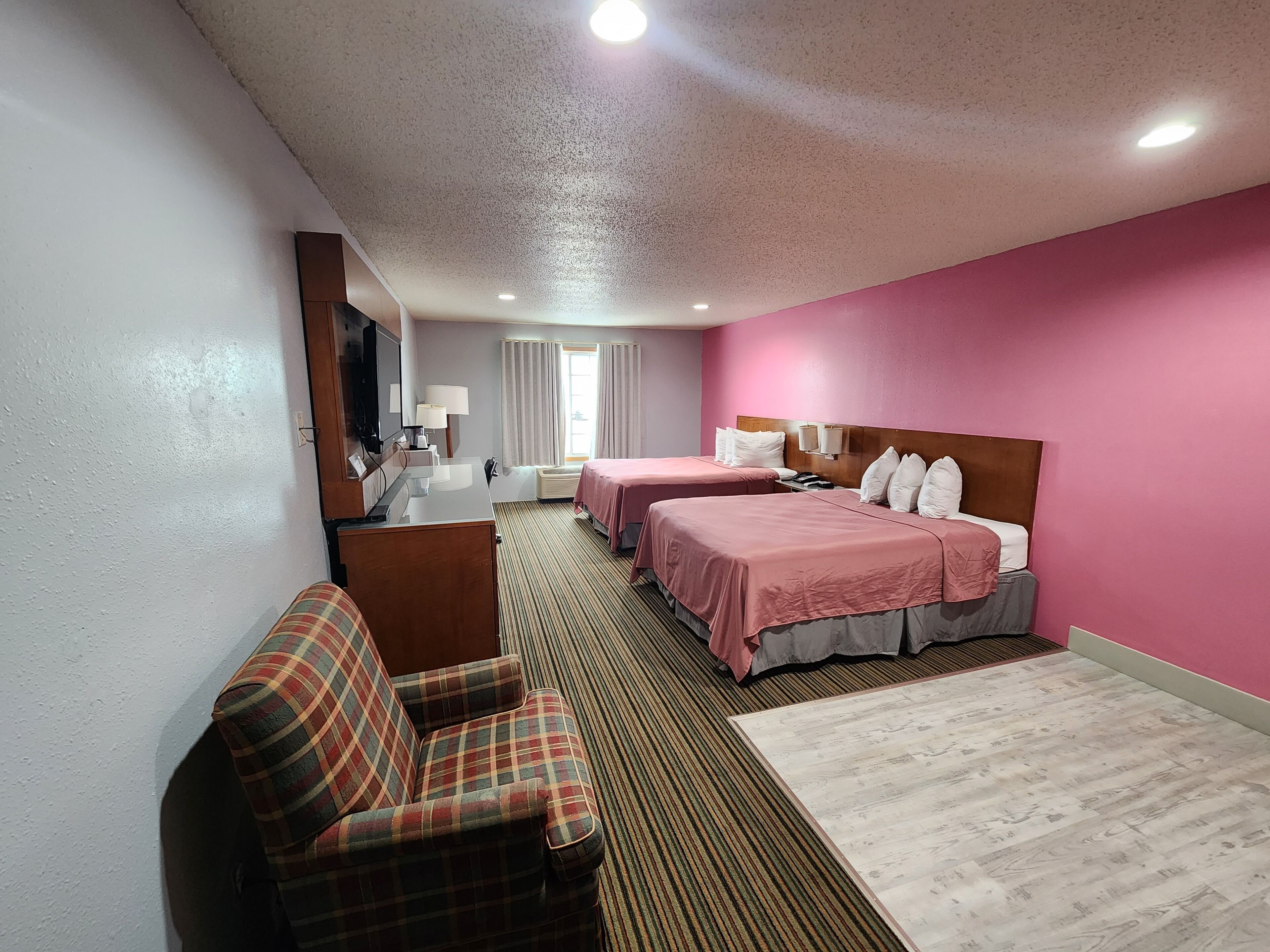 A hotel room with two beds, a sofa, a desk, and a television.