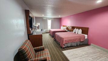A hotel room with two beds, a sofa, a desk, and a television.