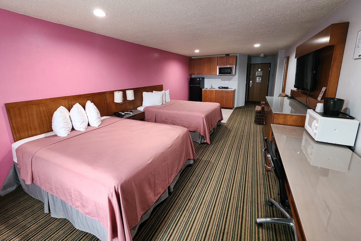 A hotel room with two beds, a kitchenette, a microwave, and a television.
