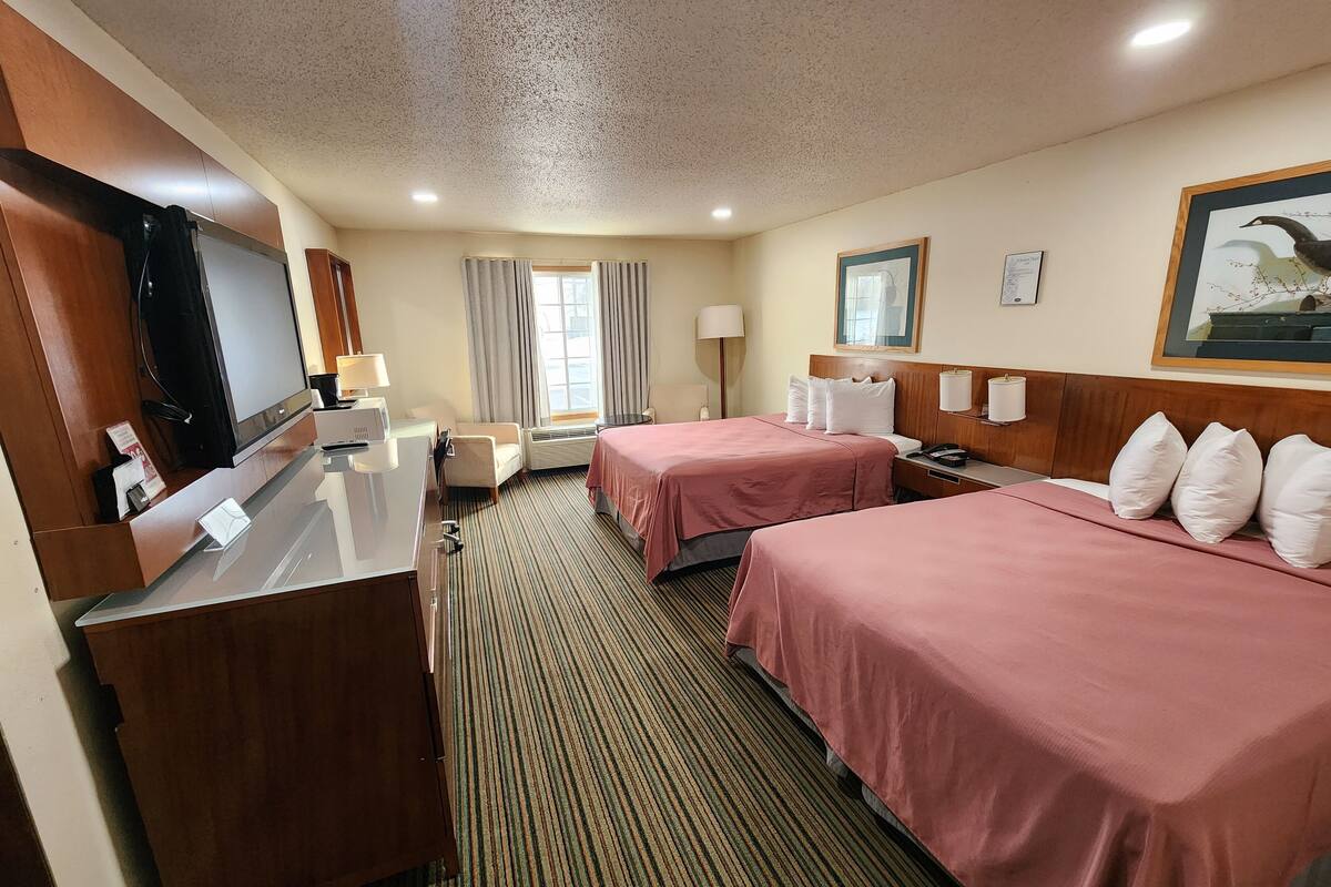 A hotel room with two beds, a desk, a television, and a window with curtains.
