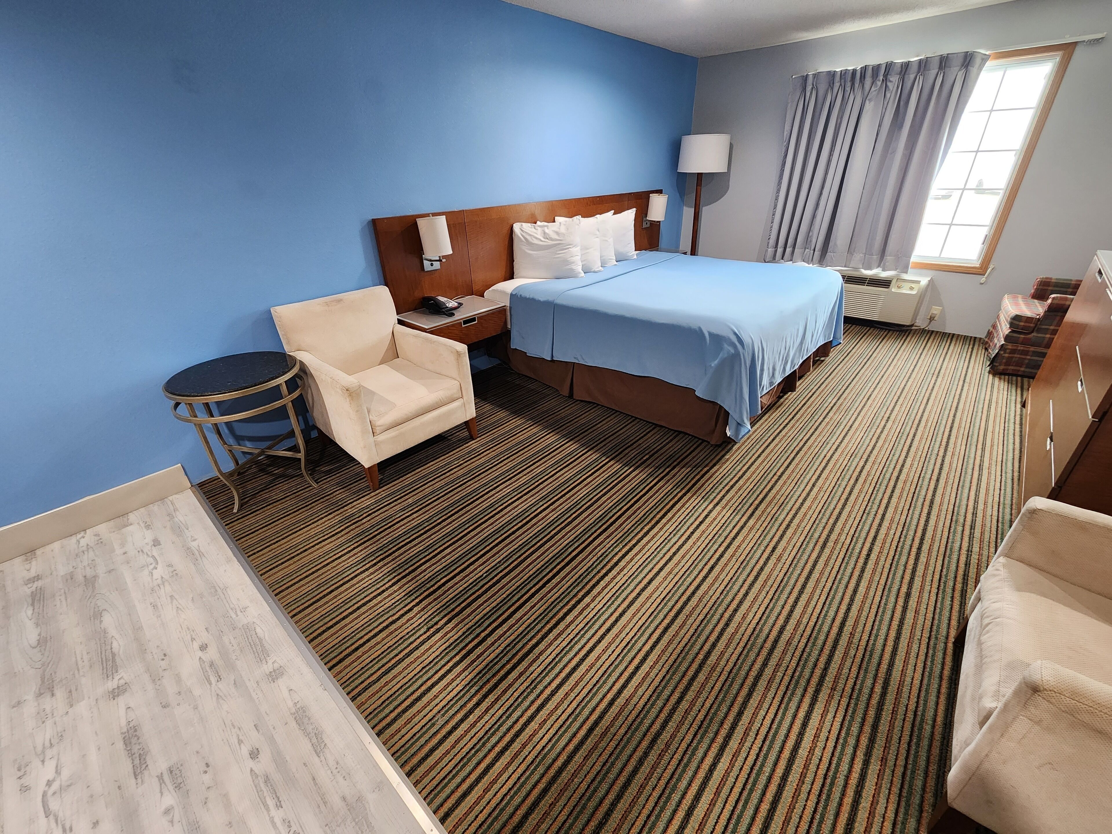 A hotel room with a bed, a chair, a desk, and a window with curtains.