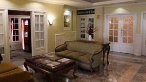 A lobby with a sofa, a coffee table, and a door leading to a restaurant. - Hotel Chester (Starkville)