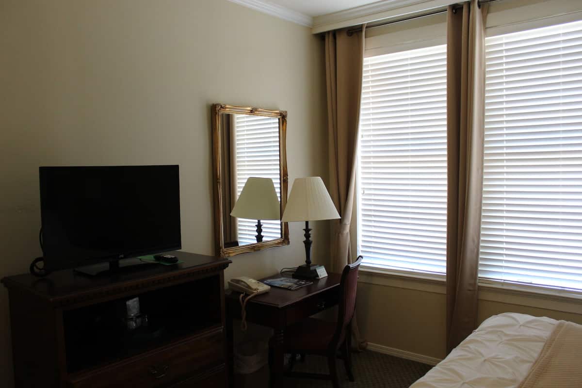 Une chambre d’hôtel avec un téléviseur posé sur un meuble en bois, un bureau avec une lampe, une chaise et un lit.