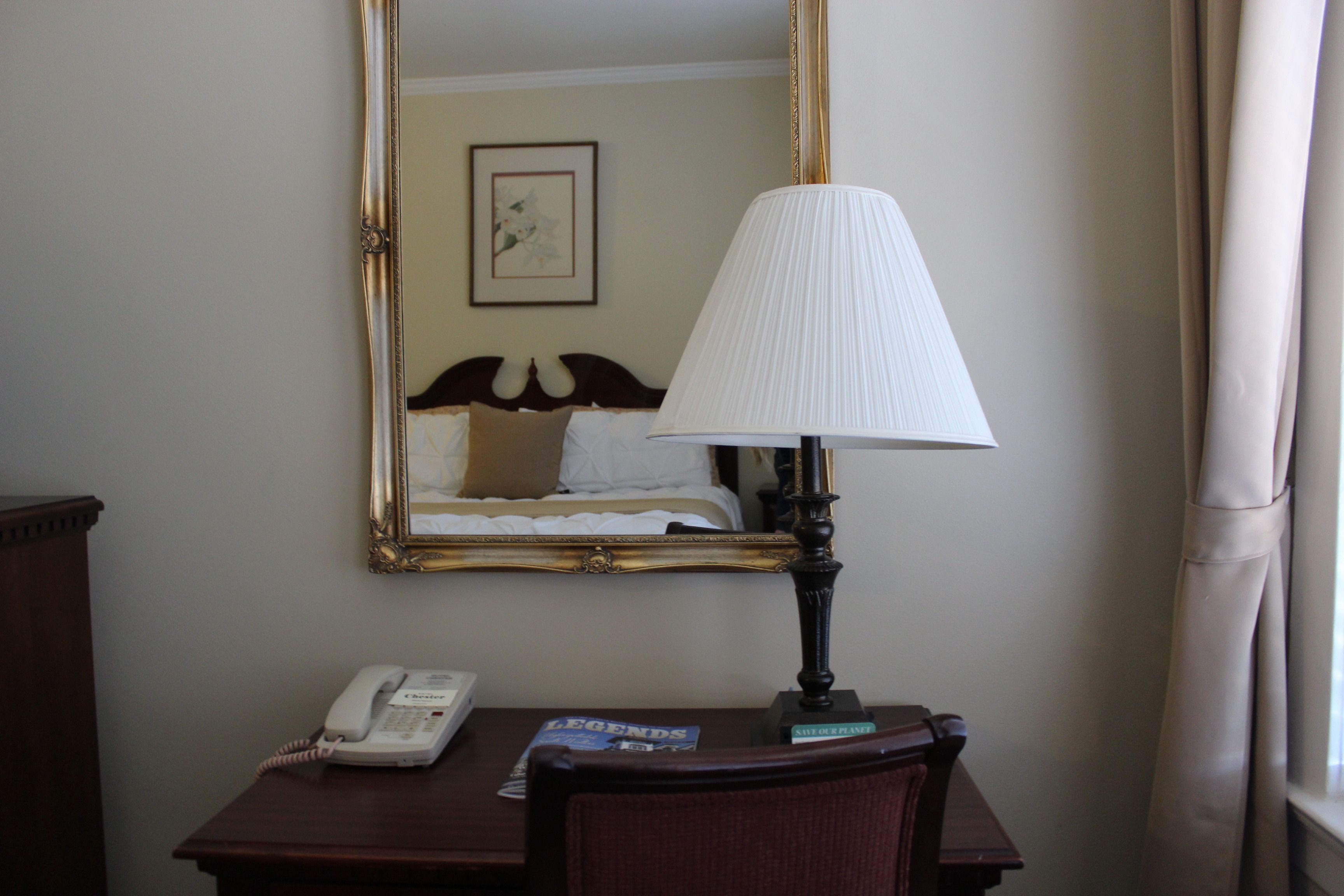 A hotel room with a bed, a bedside lamp, a telephone, and a magazine on a wooden table.