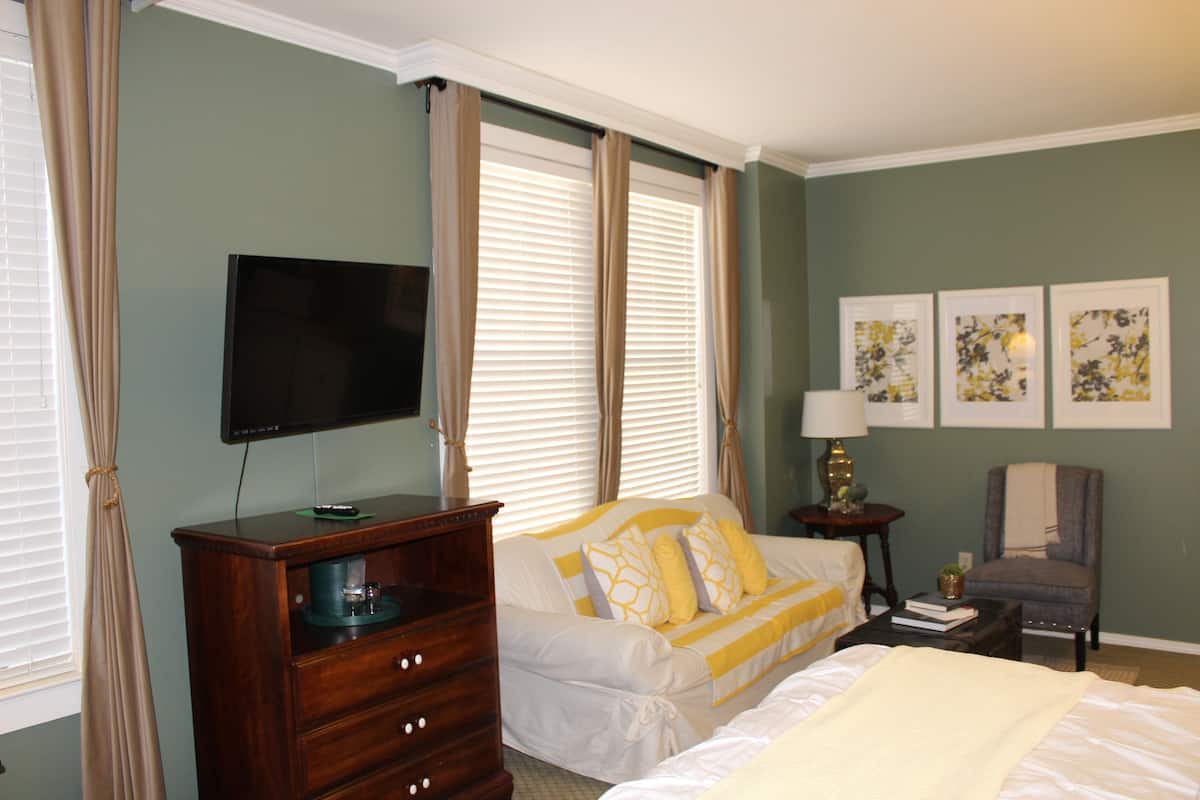 Une chambre à coucher comprenant un lit, une commode, un téléviseur, une chaise et des œuvres d’art accrochées au mur.