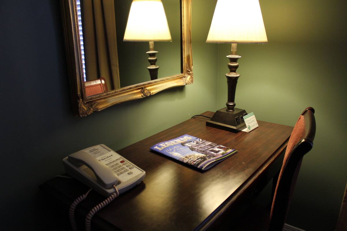 Une chambre d’hôtel avec un bureau en bois, un téléphone, un magazine, une lampe et un miroir.