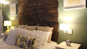 A neatly made bed with multiple pillows, a bedside table with a lamp, and a clock. - Hotel Chester (Starkville)