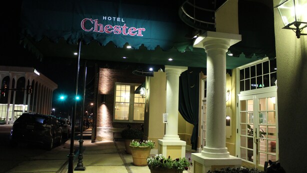 A hotel entrance with a sign reading "Hotel Chester," a covered walkway, and a street with parked cars. - Hotel Chester (Starkville)