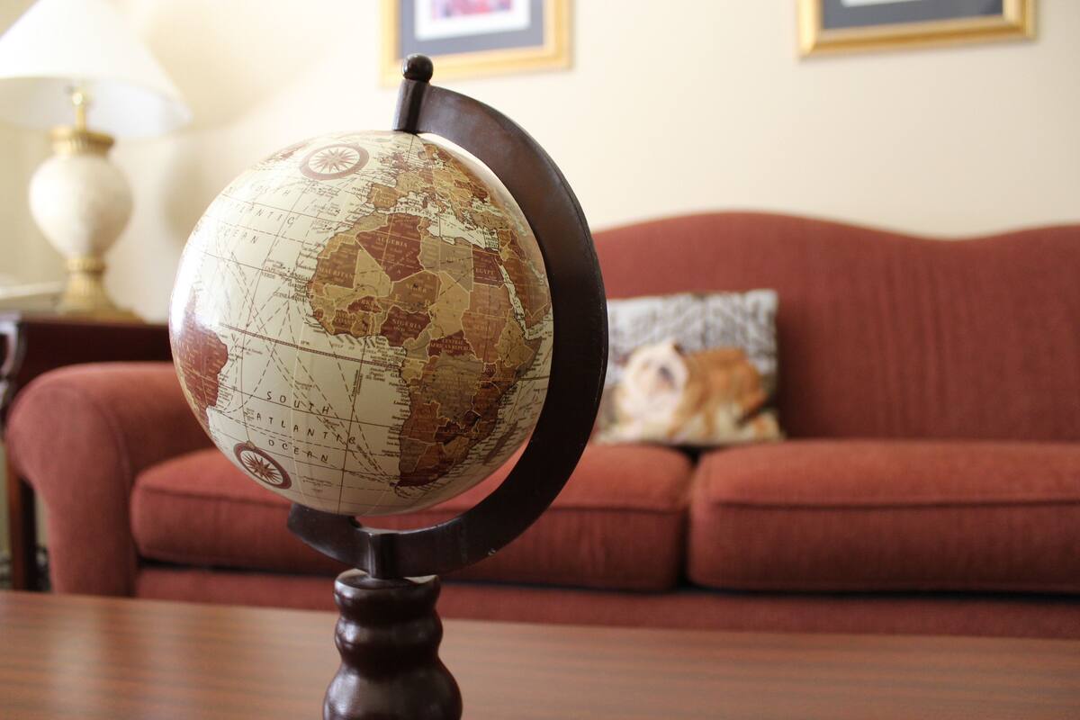 Un globe terrestre posé sur un support, dans une pièce où se trouvent un canapé rouge et un tableau encadré accroché au mur.