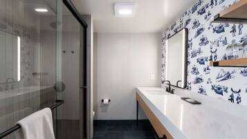 A modern bathroom with a glass shower enclosure, a white sink with a mirror, and a patterned wall.