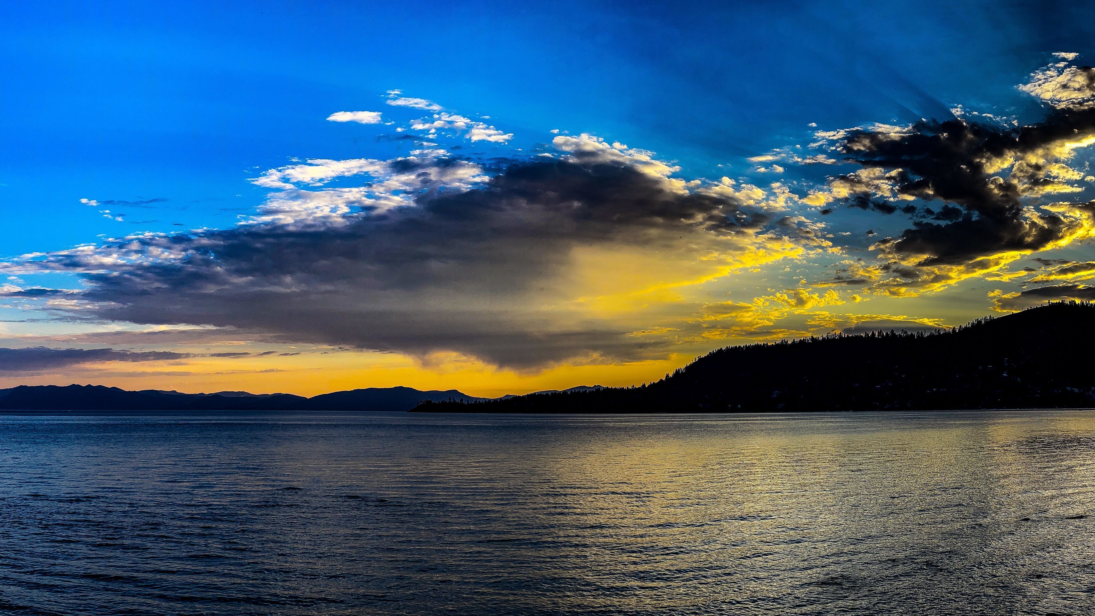 A calm lake with a mountain range in the background and a sunset sky.
