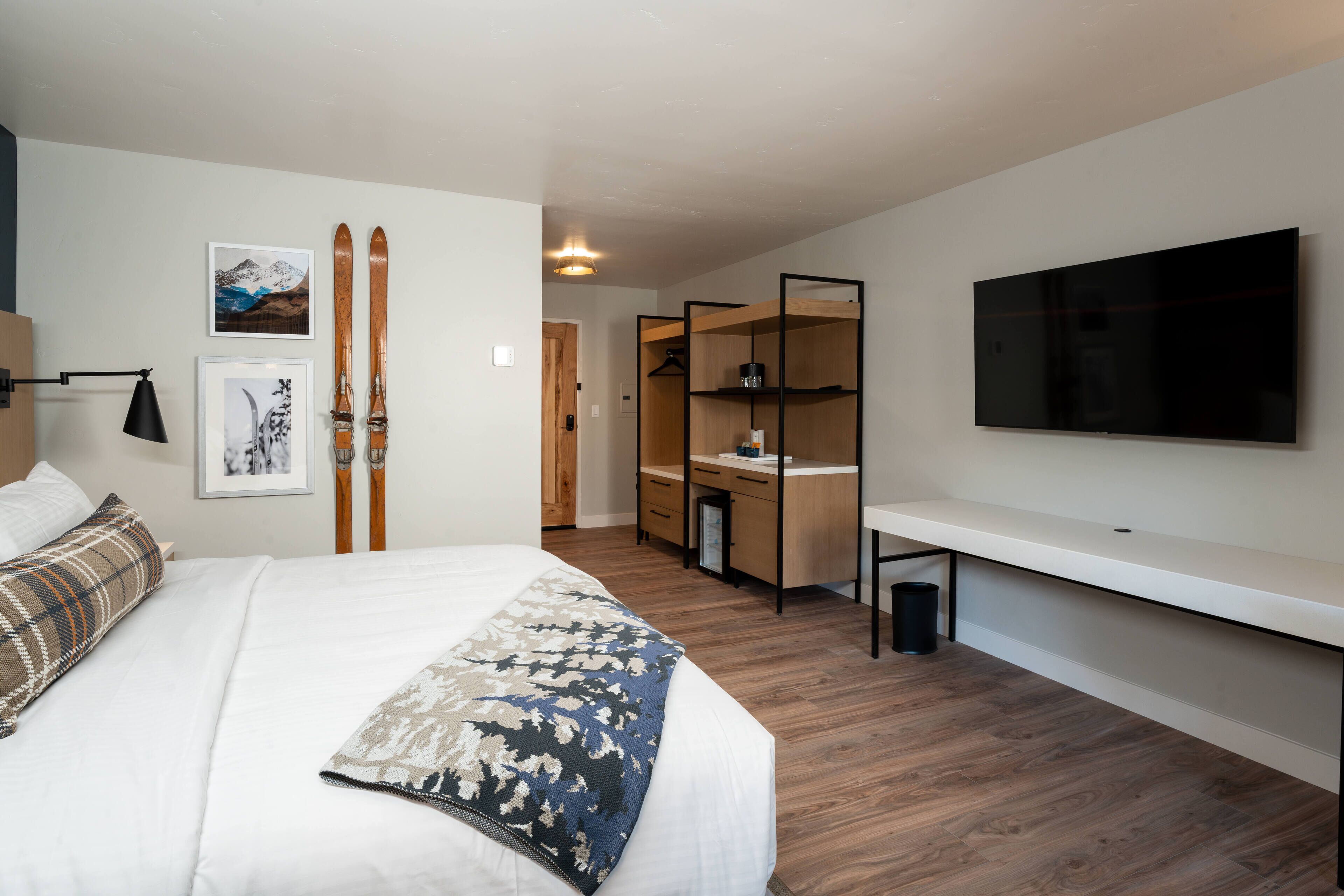 A modern bedroom with a large bed, a TV mounted on the wall, and a wooden wardrobe.