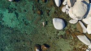 An aerial view of a beach with clear water, large rocks, and a person standing on the shore.