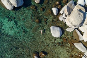 An aerial view of a beach with clear water, large rocks, and a person standing on the shore.