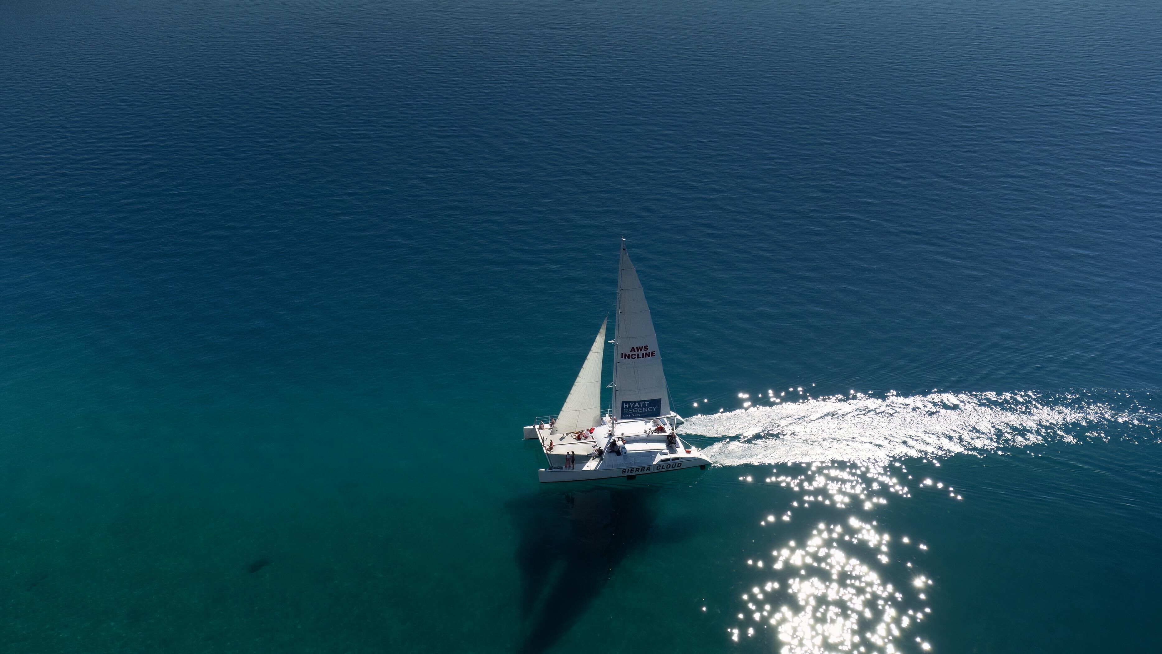A sailboat with "AWS INCLINE" and "HYATT REGENCY" on its sails, sailing on clear turquoise waters.