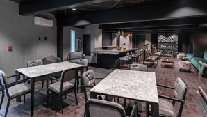 A modern restaurant with marble tables and cushioned chairs, a bar area, and a green sofa.