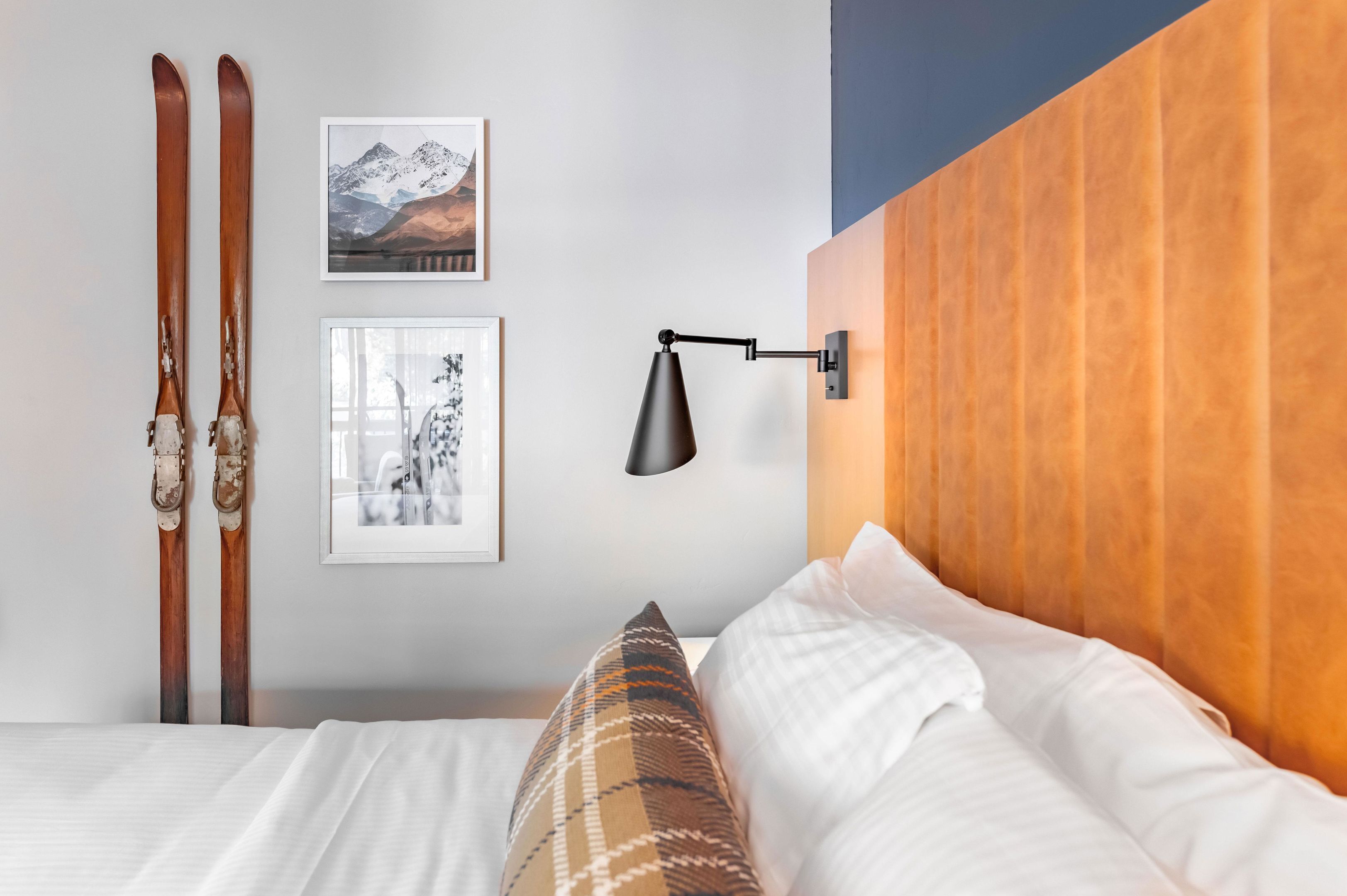 Un dormitorio con cabecera de madera, cama con ropa de cama blanca, almohada de cuadros y dos cuadros enmarcados en la pared.