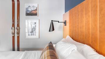 Un dormitorio con cabecera de madera, cama con ropa de cama blanca, almohada de cuadros y dos cuadros enmarcados en la pared.