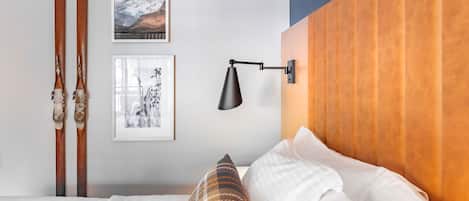 A bedroom with a wooden headboard, a bed with white bedding, a plaid pillow, and two framed pictures on the wall.