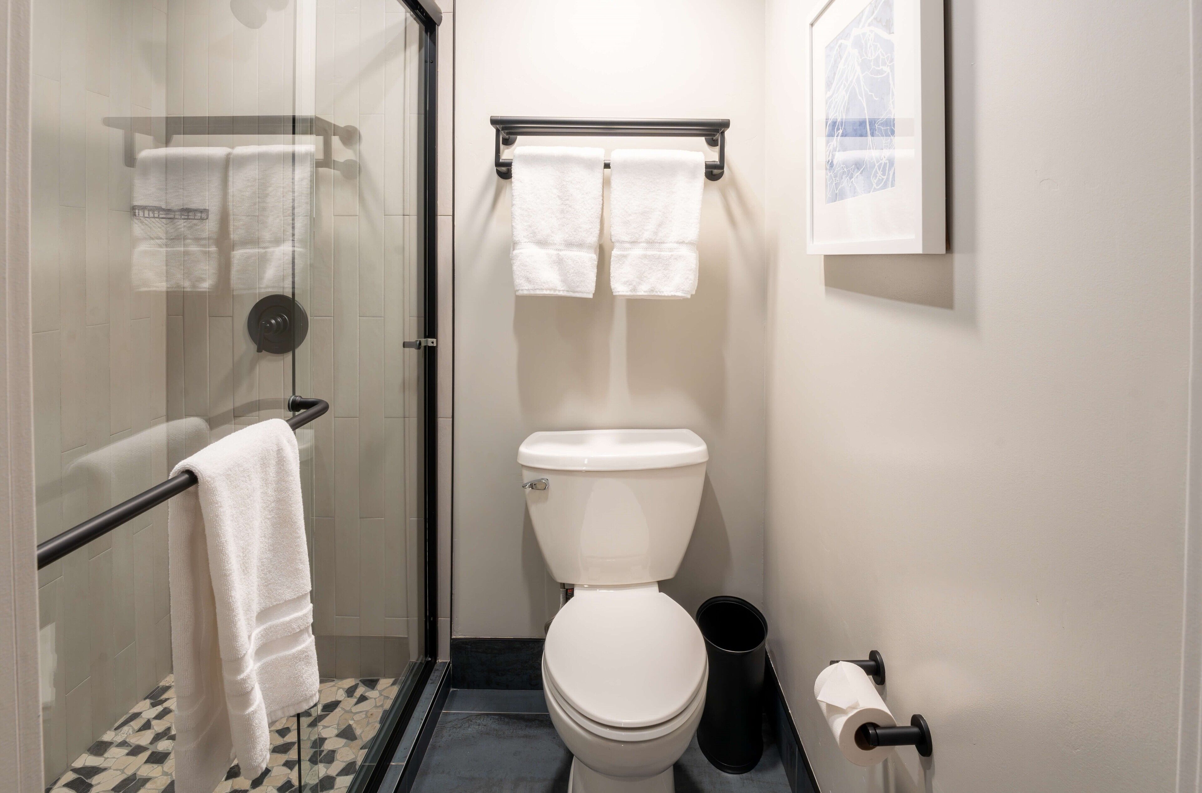 Un bagno compatto con box doccia in vetro, un WC e un cestino nero.