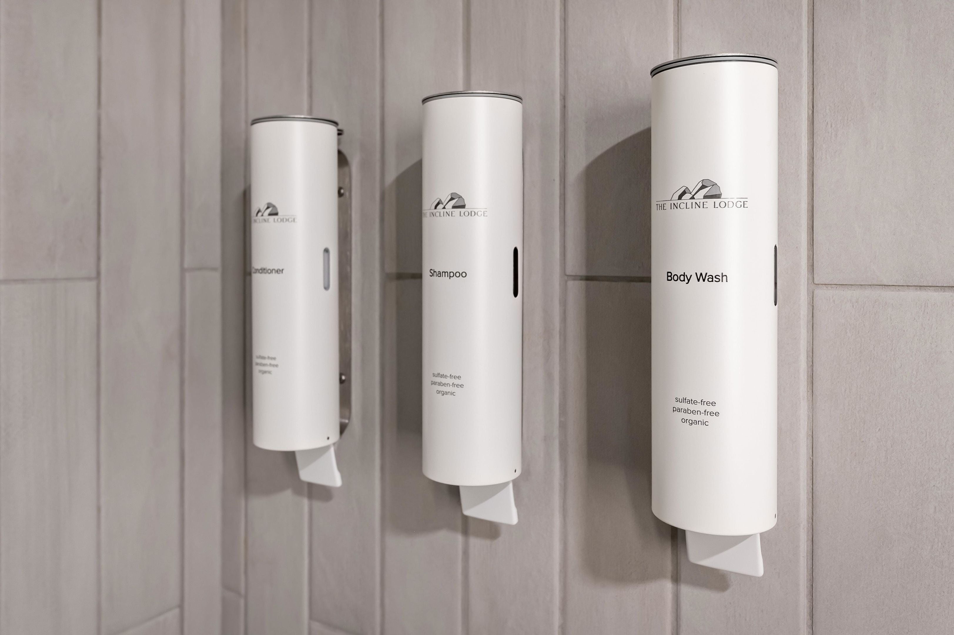 Three white dispensers labeled with The Incline Lodge branding, including a body wash, shampoo, and conditioner.