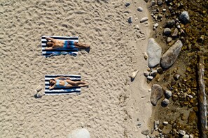 Two people lying on striped towels on a sandy beach with rocks.