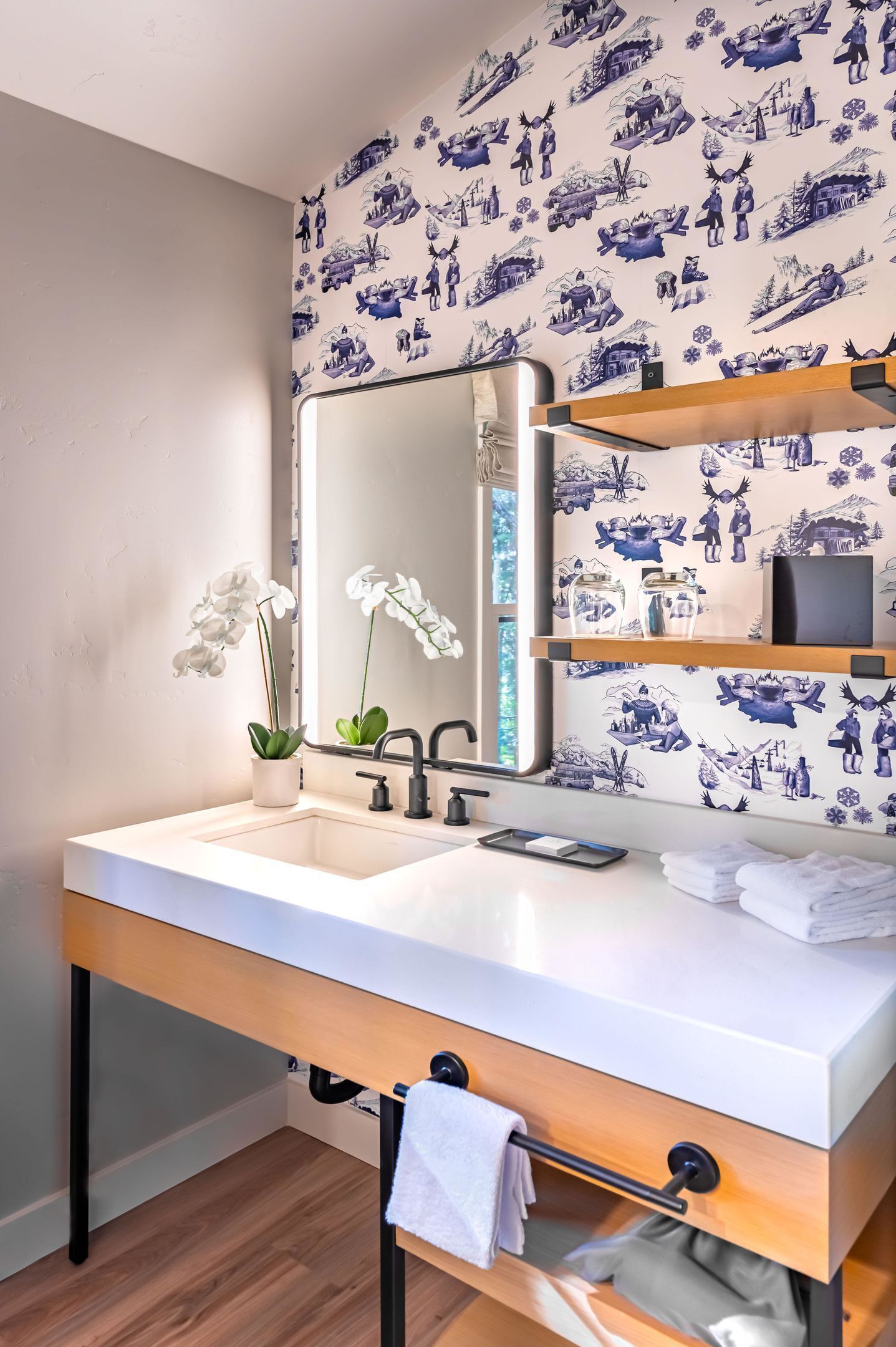 A modern bathroom with a white sink, black faucets, a mirror, and a wooden vanity with a towel rack.