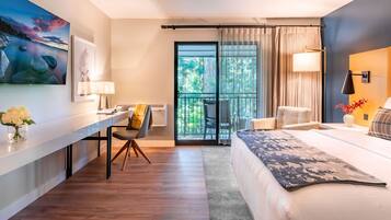 A modern hotel room with a bed, a desk, a chair, a balcony with curtains, and a painting on the wall.