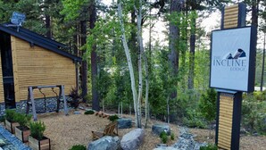 A lodge with a wooden exterior, surrounded by a landscaped garden with rocks, trees, and a swing set.