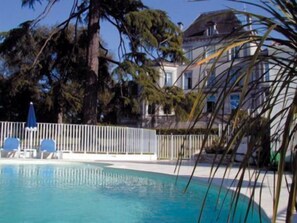 Una piscina con cerca blanca, palmeras y un edificio al fondo.